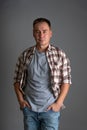 A man in a plaid shirt and a gray T-shirt stands against a gray background with his hands in his pockets Royalty Free Stock Photo
