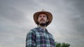 Man in plaid shirt holding spikelet, reed, dry grass his mouth and looking away while standing