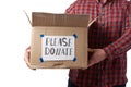 Man in a plaid shirt and jeans holds a brown cardboard box with the inscription please donate Royalty Free Stock Photo