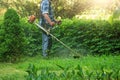 Man in a plaid shirt with a manual lawn mower mows the grass in city park