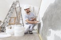 Man plasterer construction worker at work, takes plaster from bucket and puts it on trowel to plaster the wall, wears helmet