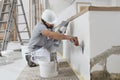 Man plasterer construction worker at work, takes plaster from bucket and puts it on trowel to plastering the wall, wears helmet Royalty Free Stock Photo