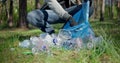 A man with a plastic bag collects garbage in the forest by impale it on a stick