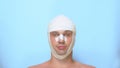 A man after a plastic surgery facelift, rhinoplasty, blepharoplasty. with a bandage on the nose, head and eyes. on blue