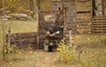 Man Player Shooting With A Paintball Gun Hiding Behind Wooden Shelter On A Playground In A Forest
