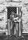 Man playing acoustic guitar in front of old country barn and American flag Royalty Free Stock Photo