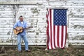 Man playing acoustic guitar standing on front of American flag hanging on old barn door Royalty Free Stock Photo