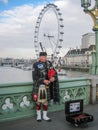 Man playing bagpipe, dressed in traditional scottish costume on banks of the River Thames