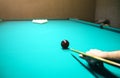 Man is playing billiard. Guy is holding pool cue in his hand. Small black cue ball is on the centre of the green table. Sports and