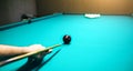 Man is playing billiard. Guy is holding pool cue in his hand. Small black cue ball is on the centre of the green table. Sports and