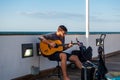 Man, with glasses and beard, playing guitar on bridge beside the beach while the sun is setting Royalty Free Stock Photo