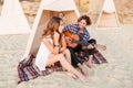 Man playing guitar for his girlfriend sitting at camping tent