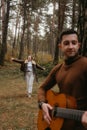 Man playing guitar outdoors in woods, woman dancing behind him in the autumn park Royalty Free Stock Photo