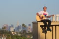 Man playing guitar on roof with LA skyline Royalty Free Stock Photo