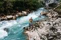 Man playing guitar standing on the bank of a mountain river on a background of rocks and forest. Handsome hippie style guitarist