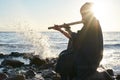 Man playing on Indian Bansuri instrument in sunshine at sea shore