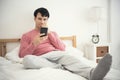 Man playing mobile phone on bed in bedroom and alarm clock Royalty Free Stock Photo