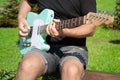 Man playing a turquoise electric guitar in a park on a sunny day Royalty Free Stock Photo