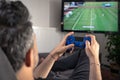 Man playing video game at home sitting on coach sofa in front of television with play game concole and joystick in hands
