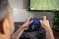 Man playing video game at home sitting on coach sofa in front of television with play game concole and joystick in hands
