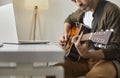 Man plays acoustic guitar at home in front of online audience or provides music lesson using laptop. Royalty Free Stock Photo