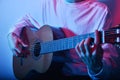 A man plays an acoustic guitar in neon red-blue light. A man learns to play the guitar, music, hobbies