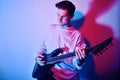 A man plays the electric guitar in neon light, red blue light. Hobbies, music, club. A man enjoys playing the guitar, screaming, Royalty Free Stock Photo