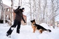 A man plays fetch with a dog in the snowy yard of a house.