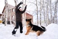 A man plays fetch with a dog in the snowy yard of a house.