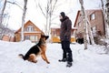 A man plays fetch with a dog in the snowy yard of a house.