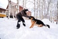 A man plays fetch with a dog in the snowy yard of a house.