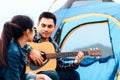 A man plays a guitar for a woman while camping beside the lake Royalty Free Stock Photo