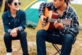 A man plays a guitar for a woman while camping beside the lake. Royalty Free Stock Photo
