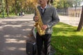 Man plays on saxophone in the park. Street musician with sax performs music for charity. Public solo performance by wind Royalty Free Stock Photo