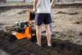 A man plows the ground with a tillerblock in the garden. Farmer man plows the land with a cultivator preparing the soil