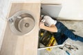 Man plumber in uniform fixing the sink with adjustable spanner in his hand lying on the kitchen floor professional