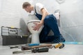 Man plumber in uniform installing toilet bowl using instrument kit professional repair service