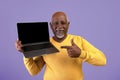 Man Points at Laptop With Empty Screen Against a Solid Purple Background in a Studio Royalty Free Stock Photo