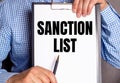 The man points with a pen to the text SANCTION LIST on a white sheet