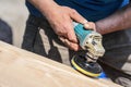 Man polishing wooden chest with old angle grinder during sunny day, closeup detail to hands without gloves, fine wood dust flying Royalty Free Stock Photo