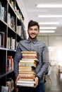 Man in portrait, college student with stack of books in library and research, studying and learning on university campus