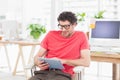 Man in red t-shirt tapping tablet, sitting in office with desks, monitors, sticky notes and plants Royalty Free Stock Photo