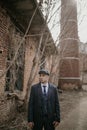 A man posing in the image of an English retro gangster dressed in Peaky blinders style near abandoned building