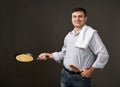 Man posing with a pancake in a pan, white shirt and pants, gray background
