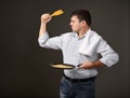 Man posing with a pancake in a pan, white shirt and pants, gray background