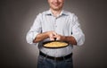 Man posing with a pancake in a pan, white shirt and pants, gray background, shallow depth of field, sharp pancake and blurred face