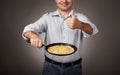Man posing with a pancake in a pan, white shirt and pants, gray background, shallow depth of field, sharp pancake and blurred face