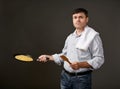 Man posing with a pancake in a pan, white shirt and pants, gray background, surprised emotions