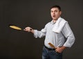 Man posing with a pancake in a pan, white shirt and pants, gray background, surprised emotions