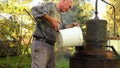 Man is pouring brandy in distillation apparatus for making domestic alcohol liquor